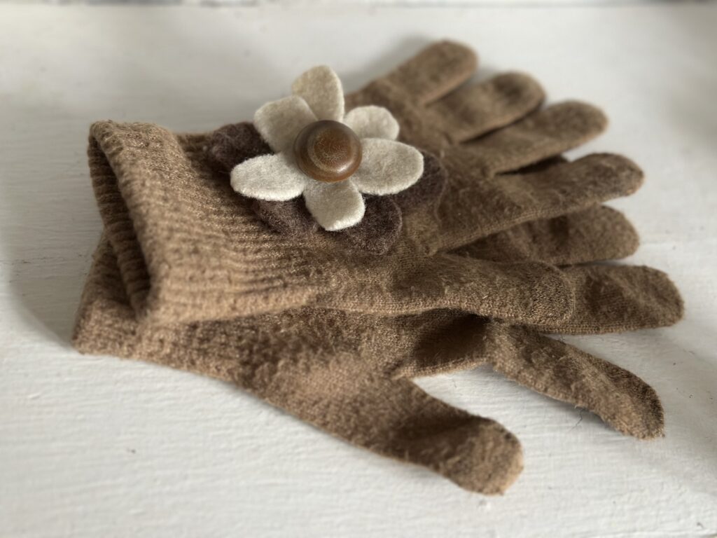 A pair of thin brown gloves with a cream and brown woolen flower. 